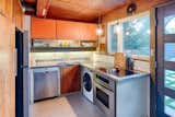 The kitchen in this home features its original cabinets, stainless-steel countertop with integrated sink. and tile backsplash. a new section of stainless-steel countertop was added on the right to replace the original range and clothes-washing machine.