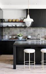 In this kitchen by DISC Interiors, the stark black cabinets and kitchen island are offset by light whitewashed floors and white-and-brass accents. To finish off the look, a patterned ceramic tile backsplash packs a punch.&nbsp;