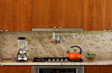The kitchen was designed to be as sleek and minimalist as possible, yet remain "warm" to the eye. Unlike a range, a cooktop and oven do not disrupt the line of the countertop.  The range hood is mostly hidden and only shows a thin horizontal line tucked within the line of the cabinets. It pulls out when in use, and slips back into line with the cabinets when not.