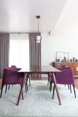 A bold and refined color palette. The dining room combines existing pieces, like the magenta mid-century chairs, with a new wooden table, for an  understated elegance. Recessed ceiling lights add a natural hue when the sun goes down.
