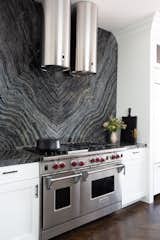 Awash in silver wave stormy marble, the backsplash makes a bold statement, while a stainless steel range creates a dramatic effect. 