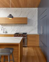 the kitchen is textured with a wall of Neolith, veins climbing as a backdrop to the warm wood.