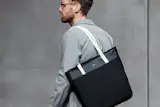 The Tokyo Tote (Premium) from Bellroy can hold an astonishing amount of goods in a sleek, simple package that can be comfortably carried over the shoulder. At 6' 3" I’ve tried other shoulder totes and the Tokyo Tote is very comfortable and can house my laptop, iPad Pro, cord management, notebooks, and more. The premium nylon and leather surfaces are built to last many, many years.

https://bellroy.com/products/tokyo-tote-premium/nylon/black_sand