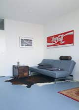 Living room sitting area. Vintage sign by Coca-Cola, an antique travel trunk, and a ‘Splitback’ sofa bed by Innovation. Cow skin rug and leather pillow by DOM. Army blanket by Merci Paris and off-the-shelf grey pillows. Lamp by MetalArte, type 'ZEN'. Black frame with digital artwork.