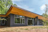 The deep, angled, wood-clad soffit is an intriguing visual and textural contrast to the dark gray cement board exterior walls. 