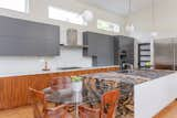 The kitchen features Kendall gray upper cabinets above a continuous row of natural walnut lower cabinets topped with white quartz. The island features Sedna granite on the top and two sides. The other two sides are white quartz. 