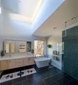 The spa-like main bathroom features a high ceiling, black floor tiles, a dual sink vanity, a deep soaking tub, and a shower with a hexagonal tile accent wall.