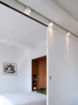 Sliding wall partially encloses bedroom, with custom designed track light fixtures above.