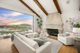 The living room features exposed beam ceilings and an oversized fireplace, with automatic walls of glass opening the space to a sweeping terrace for effortless entertaining.