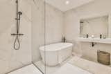 The luxury bathroom is reminiscent of a contemporary spa with elegant, light faux marble tiling, a free-standing tub, rain shower, and double vanity.