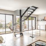 Finesse de la structure et transparence d’un escalier construit devant une large baie vitrée.
Un défi technique résolu grâce à l’implantation d’un poteau acier carré autour duquel s’enroule un hélicoïdal sur trémie carrée, qui se termine par une volée droite.
Placer un escalier contre une baie vitrée nécessite d’affiner au maximum la structure (limons et marches) en acier de 10 mm d’épaisseur.
Le résultat : une transparence douce et agréable ouvrant sur une large terrasse suspendue.

