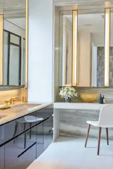 Marble and brass in the master bathroom become even more glamorous with gold-toned accents. The scheme is carried throughout with the addition of the gold and gray wallpaper reflected from the main hallway seen reflected in the vanity mirror.