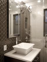 Creating a glossy modern bathroom perfect for pampering was a favorite part of this NYC apartment renovation. A gorgeous jewel box bath, it features a custom built-in vanity, vessel sink, glass shower enclosure, and ceramic wall tile in a gray and white color scheme.  Photo 2 of 16 in Bathroom by Amy from Modern Glam Apartment Renovation