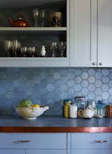 Cornflower blue hexagonal tiles form the backsplash in this blue kitchen, where the tiles continue onto the countertop (often a great way to save on your budget), which is edged in copper. The blue cabinets are a solid color in contrast to the variegated tones of the tiles.