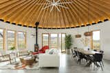 The largest of the three yurt structures houses the living and dining rooms and provides panoramic views. A geometric hide rug by Dedalo Rugs ties in pops of red from Eero Saarinen's Womb Chair, and pale blue from the Room and Board cushions on the sofa. The homeowners sourced the Oggetti Showtime coffee table from Wayfair. A pair of Kichler pendants define the dining area.