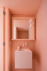 In a 1930s home in Australia, a bungalow gets a renovation including new bathrooms. A monochromatic powder room in pinky-orange features a wall-mounted sink and mosaic tile with matching grout.