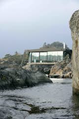 Balancing on irregular, rough-hewn rocks along the Norwegian coast, this renovated summer cabin near a town called Larvik in Vestfold County intelligently navigates a challenging terrain to take full advantage of dramatic views.
Located just about 16 feet from the sea, Lille Arøya—a 807-square-foot summer cabin—perches on a small, rugged island.
Oslo-based practice Lund Hagem Architects took on the challenge, drilling solid galvanized steel columns straight into the rock to provide stable support for the house on the uneven ground. They built a new structure that consists of two volumes:a lower post-and-beam volume where the bedrooms and bathrooms are located, and a taller volume with a large, cantilevered roof with wind-bracing gables that serves as shelter for the living, kitchen, and dining areas.
Glulam beams are used inside and out, and both interior and exterior walls are clad in rough sawn ore pine. Together with the raw steel columns and white concrete fireplace, the wood defines the color and mood of the interiors. The uniform aesthetic of the cabin's interior and exterior dissolves the threshold between indoor and outdoor spaces—and further connects the structure with its stunning, coastal landscape.
