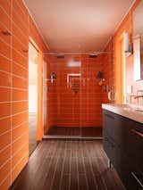 Roca wall tiles in an orange hue called Rainbow Azul were used along the walls and in the shower stall of this bathroom to give it chic midcentury vibe.