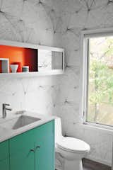 When upgrading this 1960s midcentury home in Austin, Texas, local architects local architects Rick and Cindy Black created a new powder room with punchy Jill Malek wallpaper, a turquoise built-in cabinet and vanity support, and a mirrored shelving unit with a back wall painted orange-red.