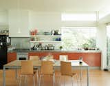 New Zealand architect Gerald Parsonson and his wife, Kate, designed their vacation beach home in Paraparaumu with an open-plan kitchen with open shelves, bar light bulbs, and bright orange MDF cabinets.