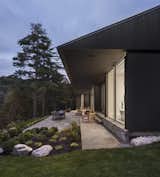 Outdoor, Large, Trees, Grass, Back Yard, Gardens, Decomposed Granite, Boulders, Stone, Decking, and Shrubs A spacious outdoor deck with a path that leads down to the lake.  Outdoor Boulders Trees Decking Stone Photos from A Lakeside Retreat in Quebec Looks Sharp With a Blade-Like Roof