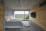 Bedroom, Track, Bed, Concrete, Wall, and Bench Kiri wood walls help keep the bedroom cool.  Bedroom Concrete Wall Track Photos from This Stacked Concrete Home Is Not Your Typical Golf Course Dwelling