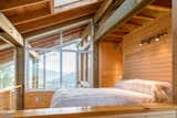 The lofted bedroom has a snug, cabin-like feel. Unfinished particle-board floors, paneled walls, and exposed wooden beams give the interior a natural and rustic feel, while large expanses of glass and clerestory windows infuse a modern vibe.