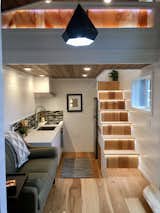 Upon entering the large glass French doors, one enters a living room with a spa-like bathroom to the left, and a drop-down galley kitchen on the right. A table and chairs slide out from the stairs to create a dining nook.  Photo 10 of 20 in This Oregon Company Crafts Exceptional Tiny Homes Starting at $40K