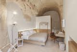 Bedroom, Bed, Night Stands, Floor Lighting, Terrazzo Floor, Lamps, and Chair Minimal furnishing conveys an aesthetic that is neutral and linear  Photo 13 of 16 in Stay in This Extraordinary Cave Hotel in Southern Italy