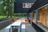 Outdoor, Shrubs, Grass, Large Patio, Porch, Deck, Trees, Wood Fences, Wall, and Vertical Fences, Wall The south-facing deck leads out to the sauna.  Photos from Two Rectangular Volumes Unite to Form a Colorful Lakeside Cabin