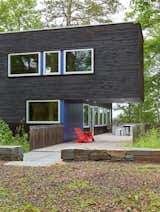 Outdoor, Wood Fences, Wall, Grass, Side Yard, Shrubs, Trees, Vertical Fences, Wall, and Large Patio, Porch, Deck The cabin's upper volume cantilevers over a wooden deck.  Photo 5 of 15 in Two Rectangular Volumes Unite to Form a Colorful Lakeside Cabin