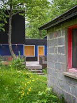 Outdoor, Vertical, Shrubs, Grass, Side Yard, Wood, Small, Trees, and Large Sections of the walls along the south-facing deck are painted bright blue to complement the sauna's pinkish-red door.  Outdoor Small Shrubs Large Photos from Two Rectangular Volumes Unite to Form a Colorful Lakeside Cabin