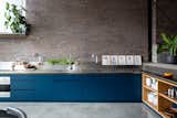 Vibrant blue cabinets brighten up this kitchen and serve as a bold contrast to the exposed brick. The stainless-steel countertop wraps slightly up the wall, and creates a trough for storing items.