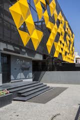 The yellow panels rest on a grey metal mesh forming the base of the façade