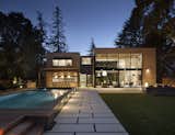 The backyard features outdoor dining, raised swimming pool, fire pit, and lounge seating. Concrete pavers provide continuity between inside and out. 
