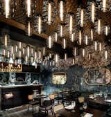 As the guests venture through the space, dense clusters of hand blown, honey coloured glass Bee Hive pendant lighting float evocatively above them.
The ceiling, treated with hand pressed brass metal in a bee wing pattern, and ensures the space is blanketed a soft, comforting amber coloured glow.
The rich narrative of the space is further articulated with Kerrie Brown, “Broken Green” wallpaper.
The pattern resonates with the memory of a 300 year old French Chateaus when the Napoleonic empire saturated Europes psyche. Brown, who designed for motion pictures, drew on her inspiration from designing films such as Don’t be Afraid of the Dark (Guillermo del Toro), Mao’s Last Dancer (Bruce Beresford), Babe for which she was nominated for an Academy Award (George Miller), The Chronicles of Narnia – The Lion the Witch & the Wardrobe & Prince Caspian (Andrew Adamson). The wallpaper appears to sit like delicate layers of a patterned midian on the wall, as if one just opened the door to a long ago abandoned building. The heavy, rich maximalist pattern of the wallpaper is accentuated by the sharp narrative of monochromatic contemporary honey comb tiles.