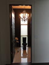 Sleek black powder room with a black toilet, black glass vanity.  Glass design vessel sink.  Bathtub chain curtain. Power room tiles from Italy and bianco damask tile niche with up lighting.  Maria Teresa chandelier with smoke crystal and matching wall sconce. 