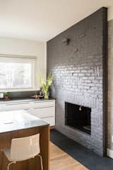 Kitchen, Wood Cabinet, Engineered Quartz Counter, Medium Hardwood Floor, and Stone Slab Backsplashe Kitchen fireplace. Original brick was damaged so it was painted dark grey. New slate hearth was added. High gloss Ikea lower cabinets are wrapped with custom white oak panels by AvenueTwo:Design.   Photos from Langley_Hawthorne Residence