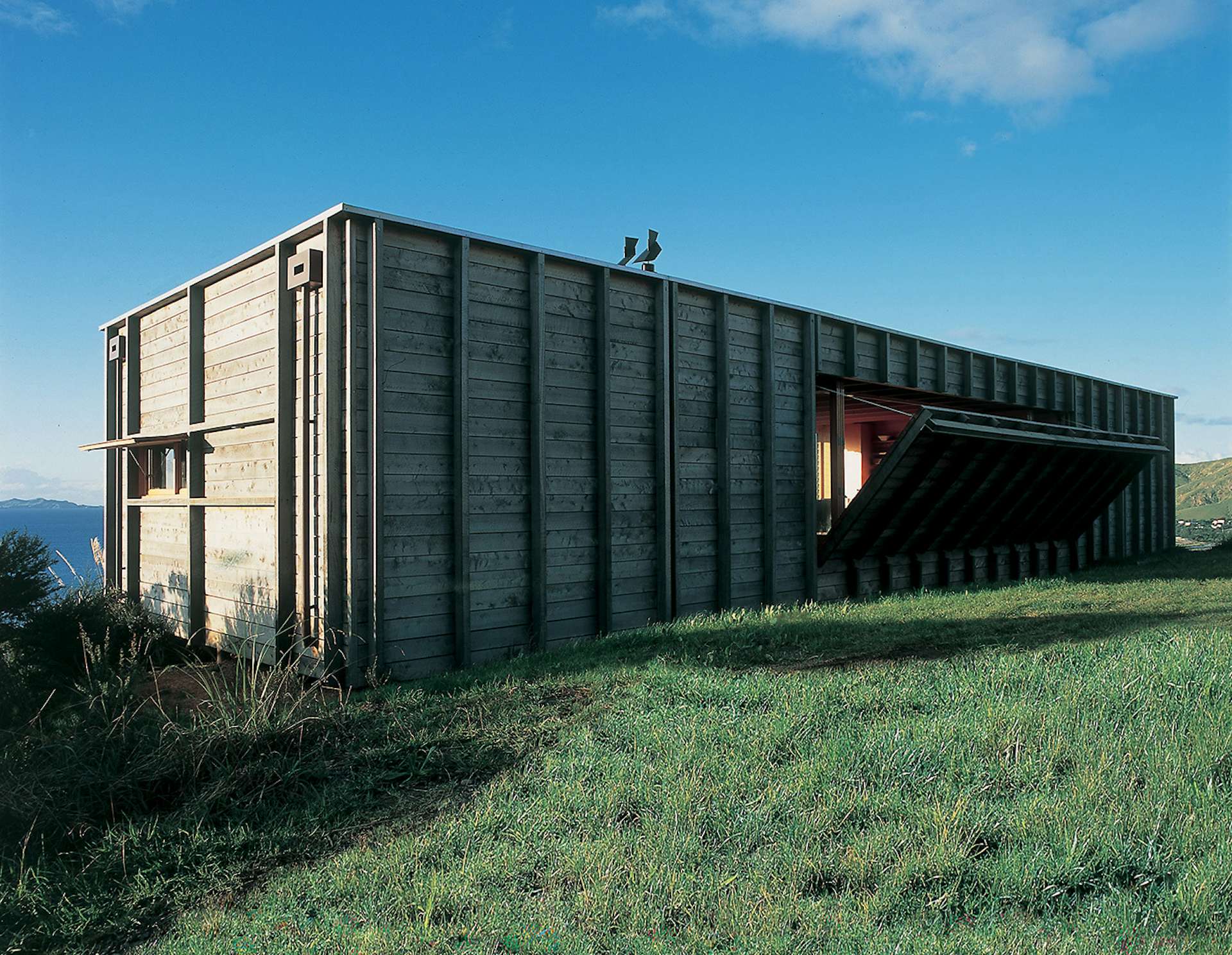 Located on New Zealand’s North Island along the Coromandel Peninsula, this timber-clad shipping container house by Crosson Clarke Carnachan Architects features a built-in mechanism that reveals a drop-down deck on one side of the unique holiday home. 