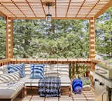 New outdoor furniture with bright blue accent pillows were chosen to perfectly complement the deep red hues of the redwood decking, railing, and shade structure. A hanging light and candle-filled lanterns further accent the space. Photo credit: Zeke Ruelas