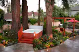 Expansive backyard featuring mature redwood trees and several signature Metamorphosis Landscaping design elements, including a hot tub feature with redwood stairs and railings, and a redwood pergola. 
