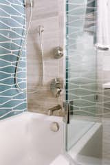 A custom swing panel glass door provides access to the shower valves without stepping into the shower or damaging the floating vanity which resides next to the tub.