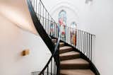 In the London neighborhood of Kenmont Gardens, a brick church's stained-glass windows provide a pop of color. It contrasts with the surrounding stark white walls and black powder-coated steel spiral staircase that connects the open-plan main level of the home to the bedrooms on the upper floors.