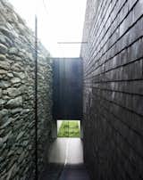 An open-air corridor is formed between the old stone walls and the new wooden shingles.