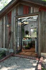 Inspired by a French farmhouse, this rustic she shed features multi-pane French doors, exposed roof rafters and joists, and earthy terra cotta floor tiles. With its wide-plank wood cladding sitting on gray stone foundations, this shed looks as though it has been around for centuries, but also has a simple, modern sensibility.