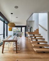 Wide-planked white oak wood flooring is echoed in both the wooden dining table and the floating wood treads of the stairs leading to the second floor.