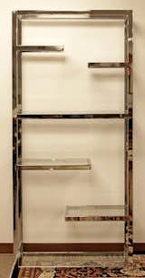 This chrome and glass etagere, or standing open shelving unit, was designed in the 1970s by famous furniture designer Milo Baughman. The etagere features four intermediate floating shelves and a central full-length shelf for bracing. The clear glass and reflective chrome make for a fun play on light.