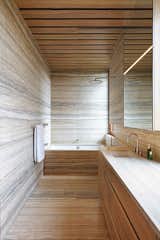 The lower-level master bath matches horizontally oriented stone with wood cabinets and drawers made from on-site trees.