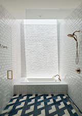 A central bathroom features a tiled bathtub under a skylight. The walls are covered in a glossy white tile, and the floors with a geometric blue and white matte tile.
