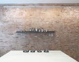 The steel shelf along the brick wall of the kitchen is made out of steel sections and holds selections of dressings, wines, salt and pepper, and wine glasses.